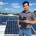 Man standing on solar panel installation, holding a inverter/controller unit on a sunny day.