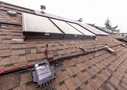 Solar panels installed on a pitched shingle roof with wiring and an electrical control box in the foreground.