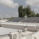 Rooftop with solar panels installed on a flat white building, with air‑conditioning units in the foreground.